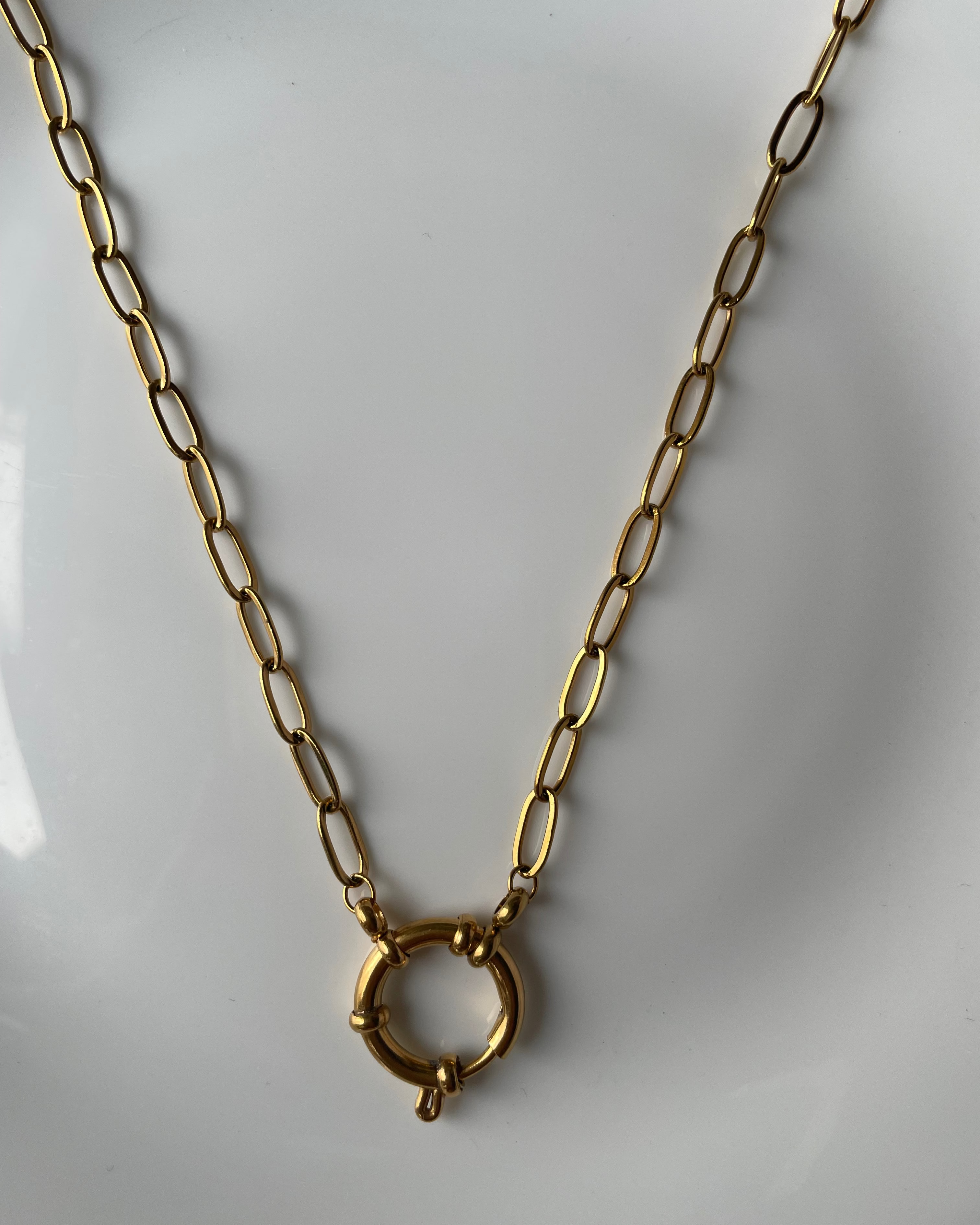 A gold paperclip chain necklace with a circular ring clasp, displayed on a plain white surface.
