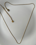 A delicate gold chain necklace with an adjustable lobster clasp and a small round disc charm, displayed on a white ceramic plate.