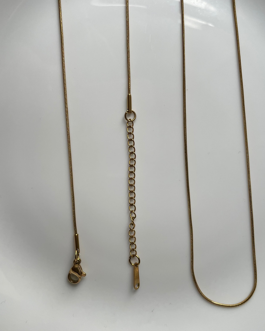 A gold-toned metal chain necklace with an adjustable extender link section, laid out on a white plate.