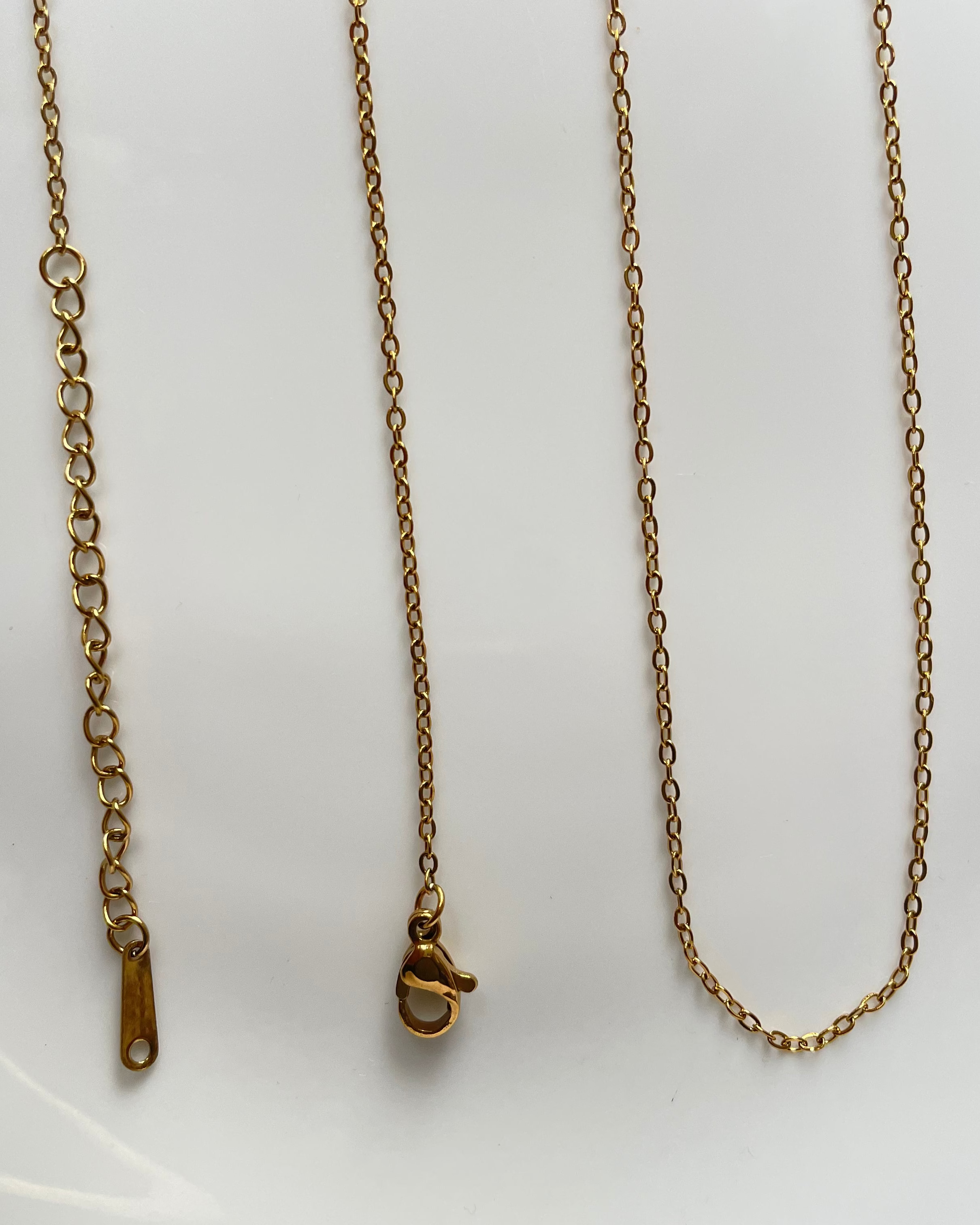 A gold-toned metal chain necklace with a lobster clasp and adjustable sliding ring extender, laid out on a plain white surface.