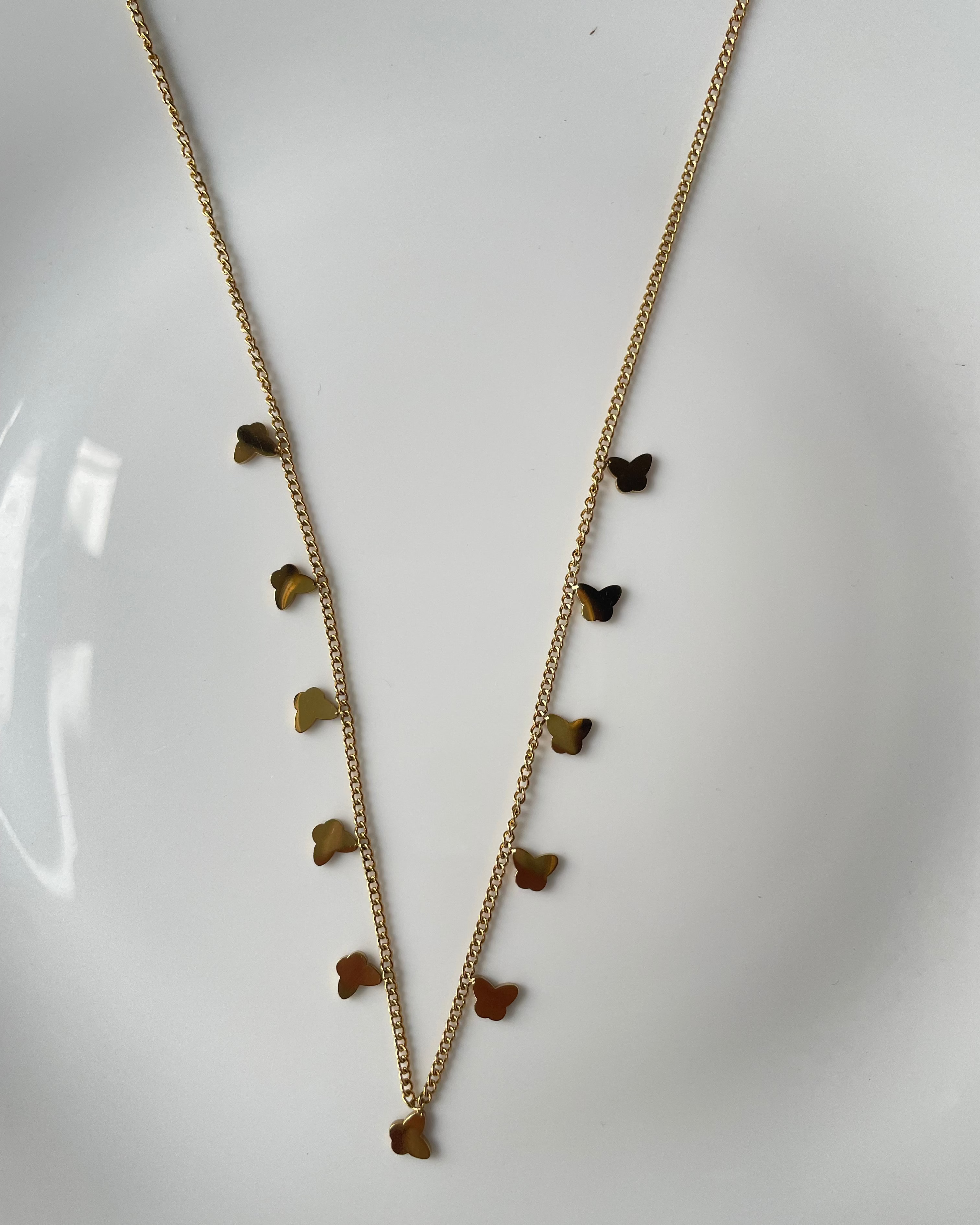 A delicate gold chain necklace featuring a series of small butterfly-shaped charms in varying shades of brown, displayed on a white surface.