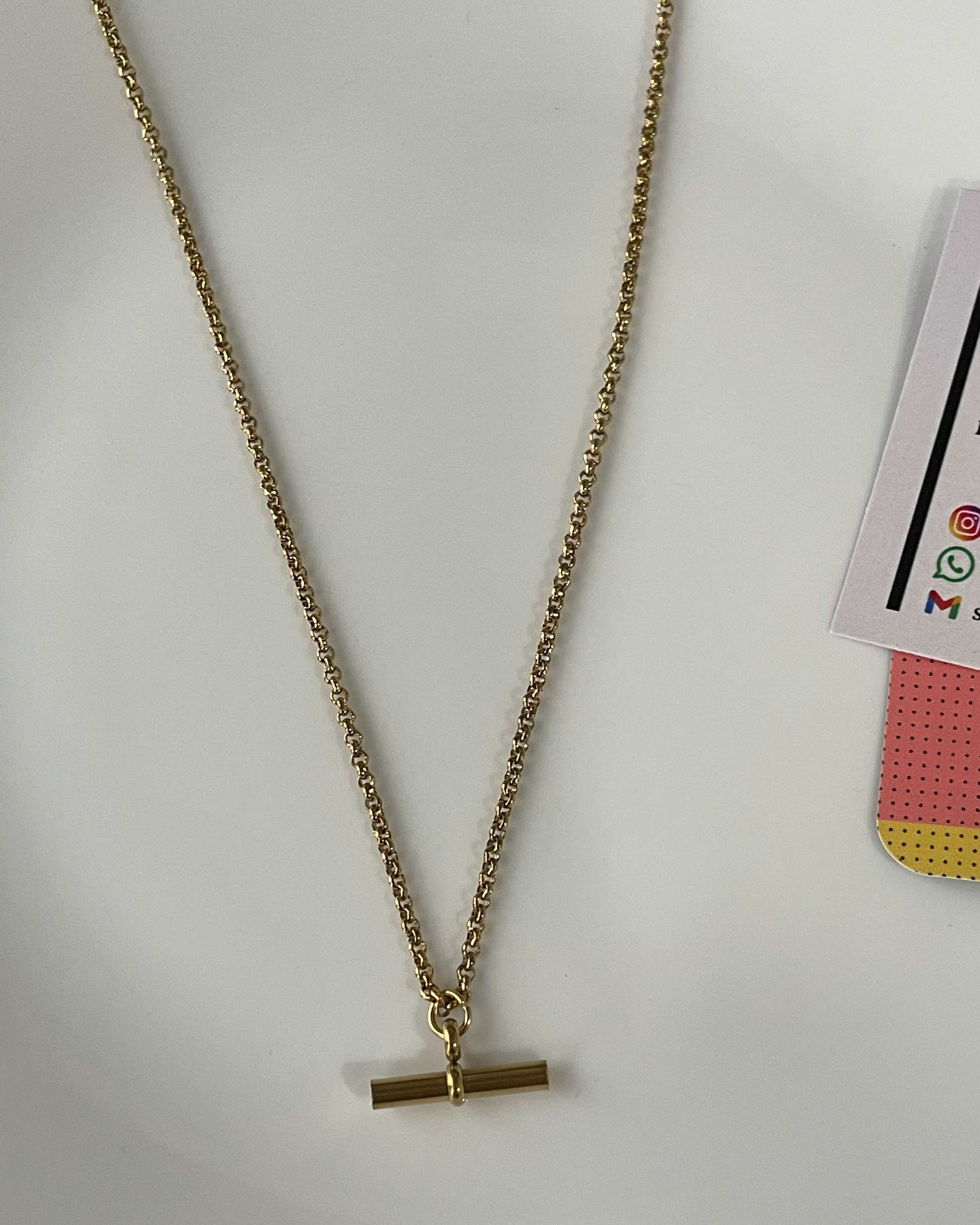 A gold chain necklace with a flat bar toggle clasp, laid out on a white surface.