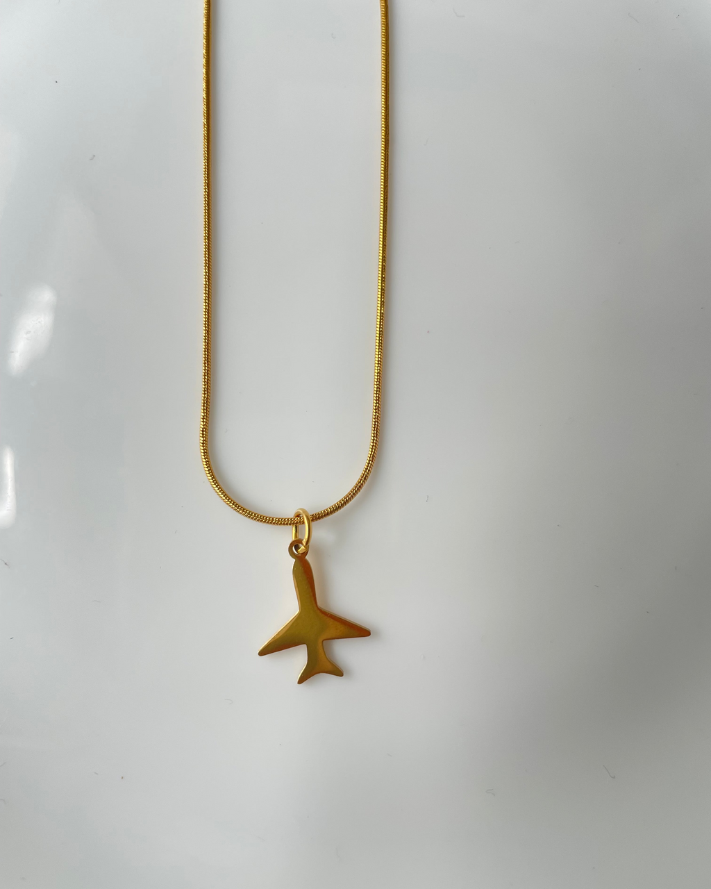 A gold chain necklace featuring a small airplane-shaped pendant, displayed against a plain white background.