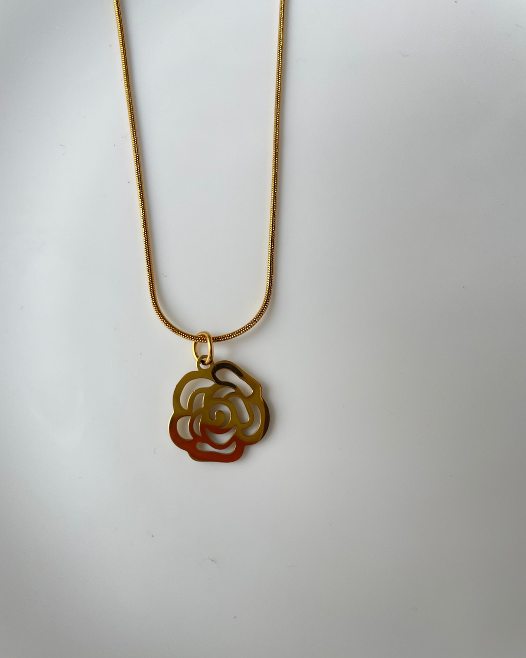 A gold-tone necklace featuring a rose-shaped pendant with a red-orange gradient accent on the lower half, displayed against a plain light gray background.