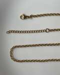 A gold-toned metal chain necklace with a lobster clasp and an adjustable sliding ring, laid out on a plain light gray surface.