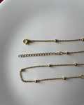 A gold chain necklace with small spherical bead details and a lobster clasp, laid out on a white surface.
