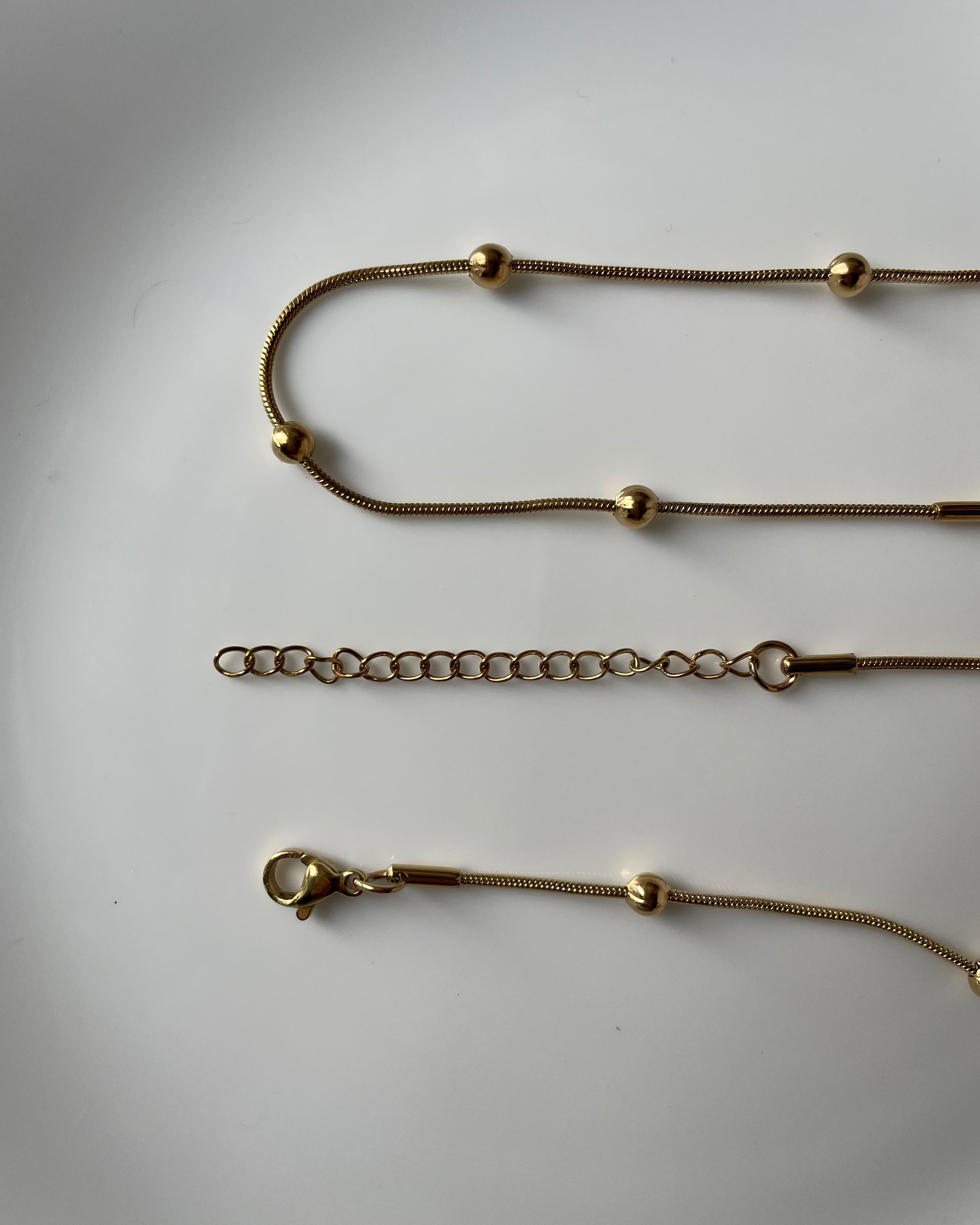 Gold chain necklace with small bead accents and an adjustable lobster clasp, shown laid flat on a light gray background.