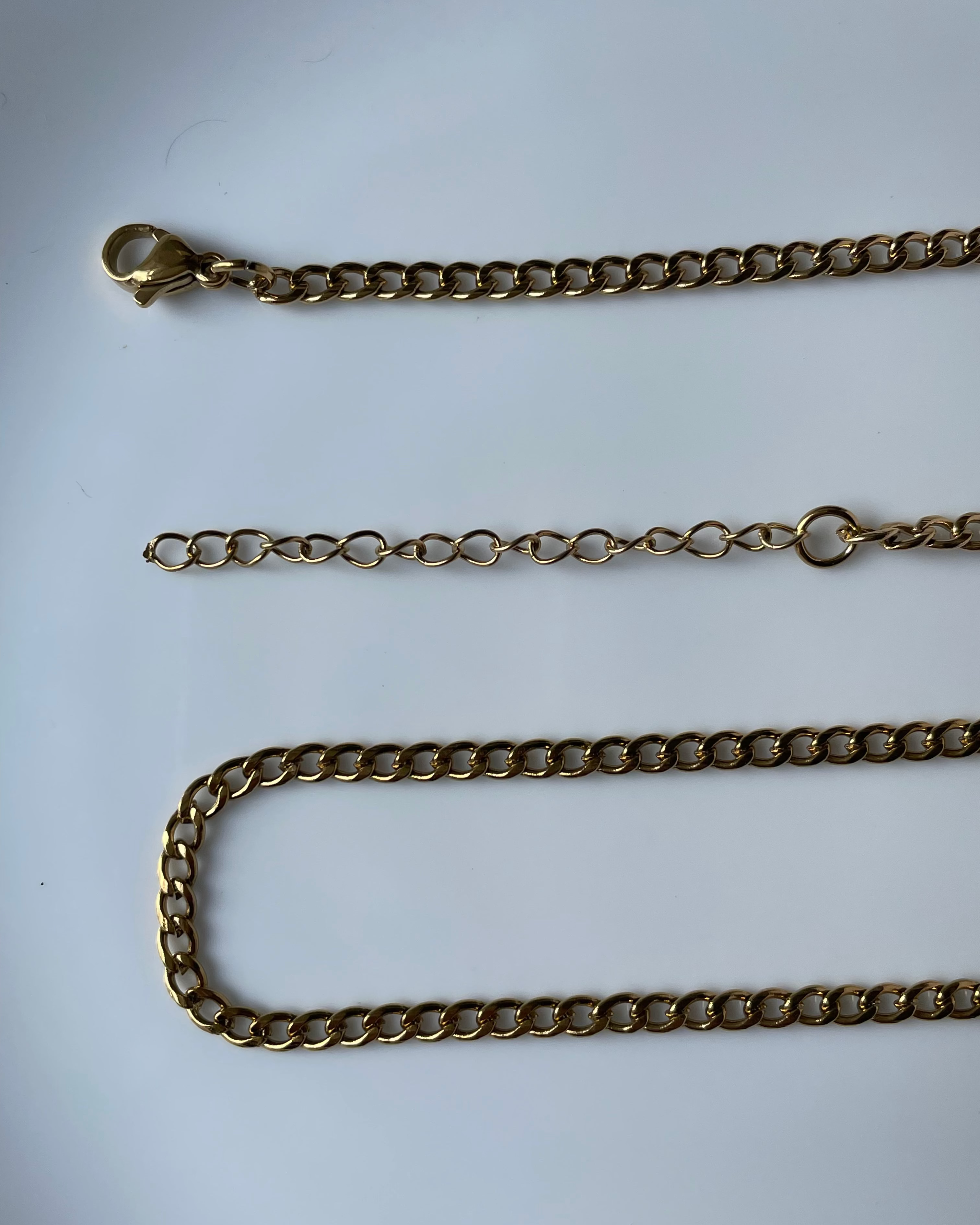 A gold-toned metal chain necklace with a lobster clasp and extender link, laid out on a plain white background.