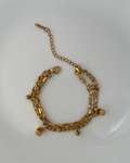 A gold-toned multi-strand chain bracelet with small bead charms and cube-shaped accents, displayed on a white plate.