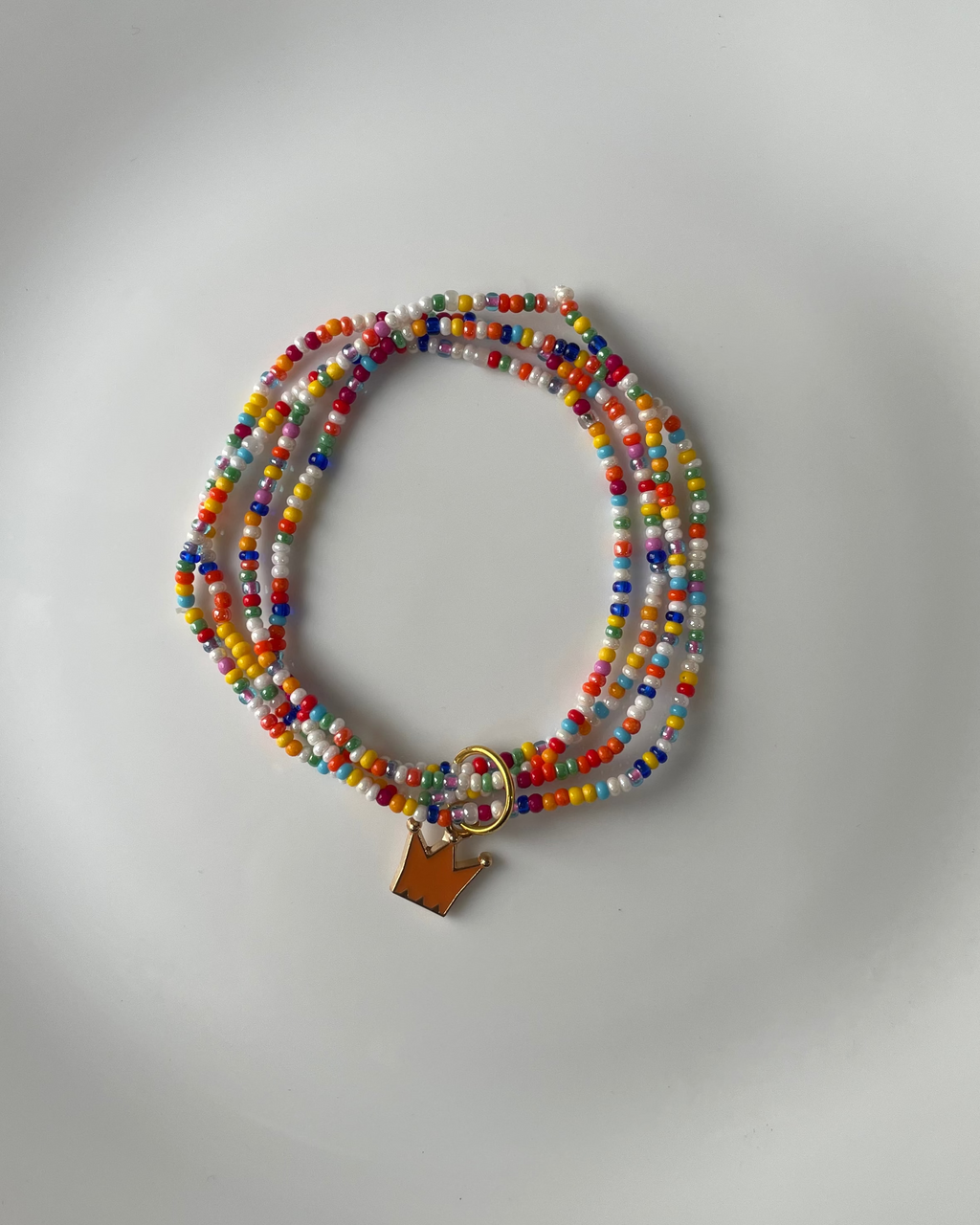 A multi-strand beaded bracelet with a small gold crown charm, displayed on a white plate.